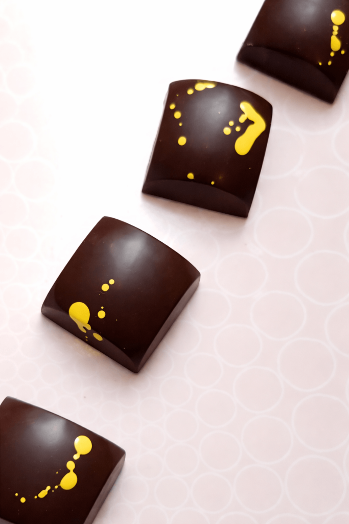 Handgefertigte Mango-Balsamico-Praline mit dunkler Schokolade und gelber Verzierung von Eve Chocolatière Tübingen