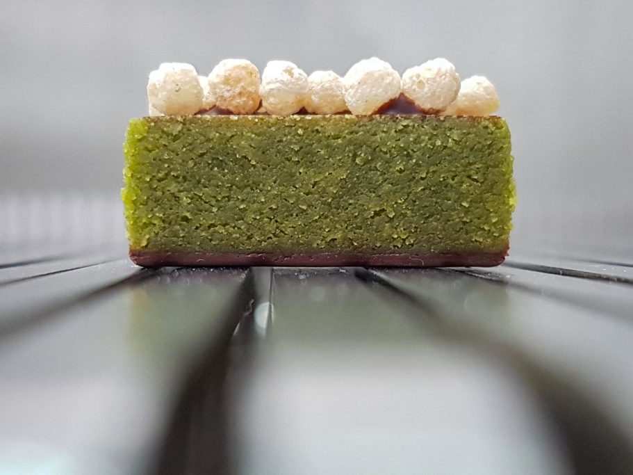 Edle Praline mit grünem Matcha-Marzipan-Kern und knusprigem Crisp-Topping auf einer feinen Schokoladenschicht